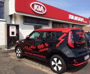 KIA Soul EV Elektroauto an Ladestation mit Werbeaufschrift: ‚100 % Elektro – Emission Impossible